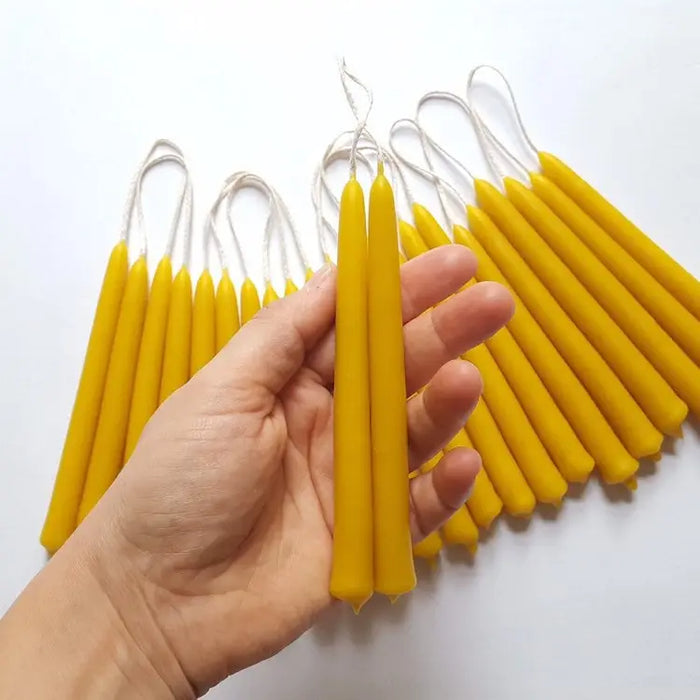 Hand holding small beeswax candles with more candles on a white background