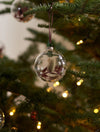 Clear glass ball ornaments with dried flowers on a Christmas tree with lights.