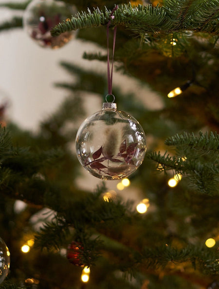Clear glass ball ornaments with dried flowers on a Christmas tree with lights.