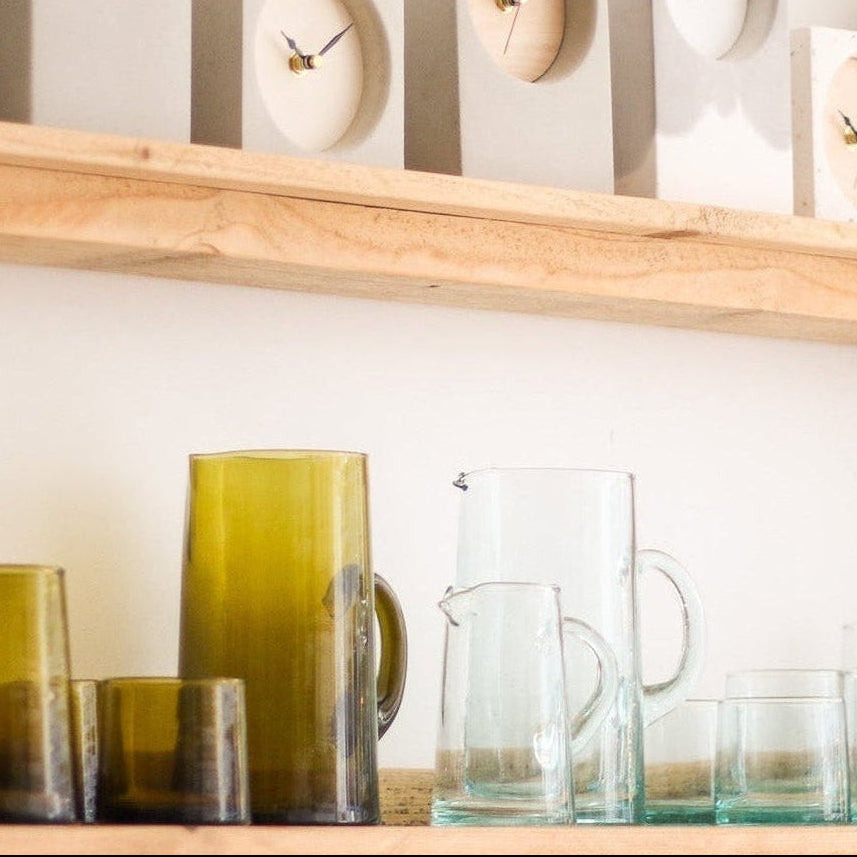 Wooden shelf with decorative clocks and glassware against a white wall