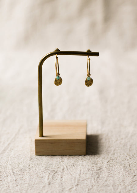 Gold earrings on a wooden stand against a beige background