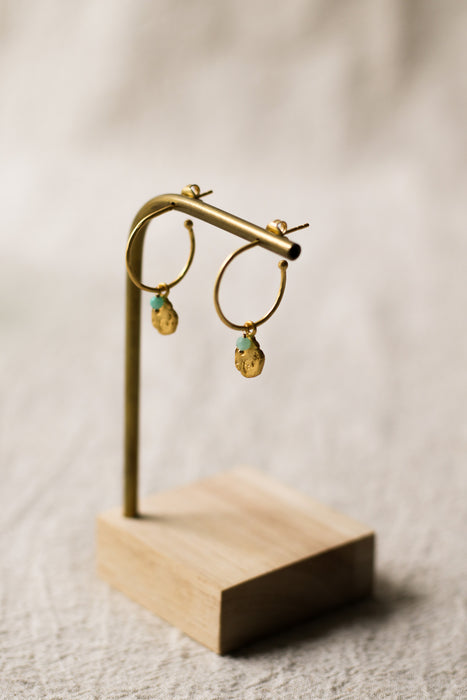 Gold hoop earrings on a wooden stand against a beige background