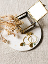 Gold hoop earrings with blue stones on a white coaster with dried flowers and a small jewellery box.