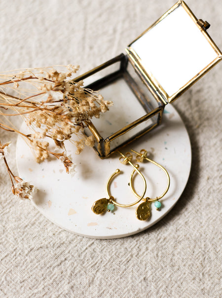 Gold hoop earrings with blue stones on a white coaster with dried flowers and a small jewellery box.