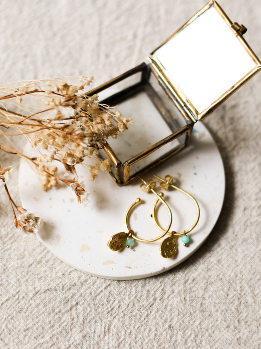 Gold hoop earrings with blue stones on a white coaster with dried flowers and a small jewellery box.