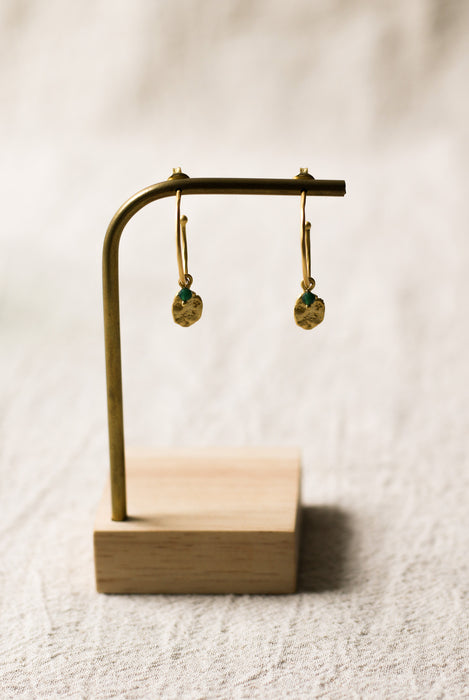 Gold earrings on a wooden stand against a beige background