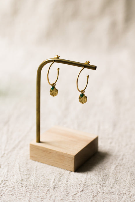 Gold hoop earrings on a wooden stand against a beige background