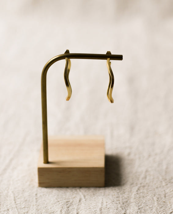 Gold hoop earrings on a wooden stand against a beige background