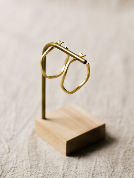 Gold hoop earrings on a wooden stand against a neutral background