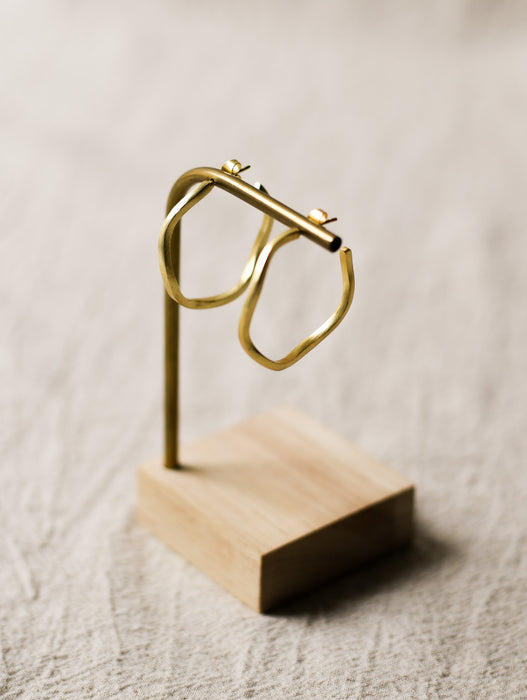 Gold hoop earrings on a wooden stand against a neutral background