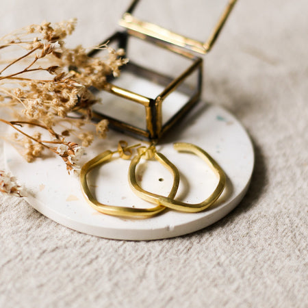 Gold hoop earrings on a white speckled coaster with a small glass jewellery box and dried flowers.