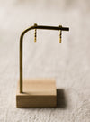 Gold hoop earrings on a wooden stand against a neutral linen background
