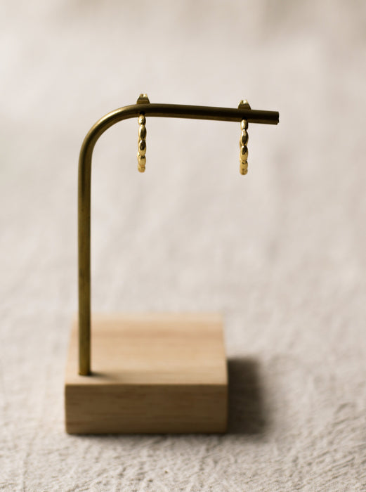 Gold hoop earrings on a wooden stand against a neutral linen background