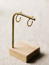 Gold hoop earrings on a wooden stand against a neutral linen background