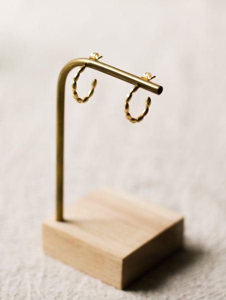 Gold hoop earrings on a wooden stand against a neutral linen background