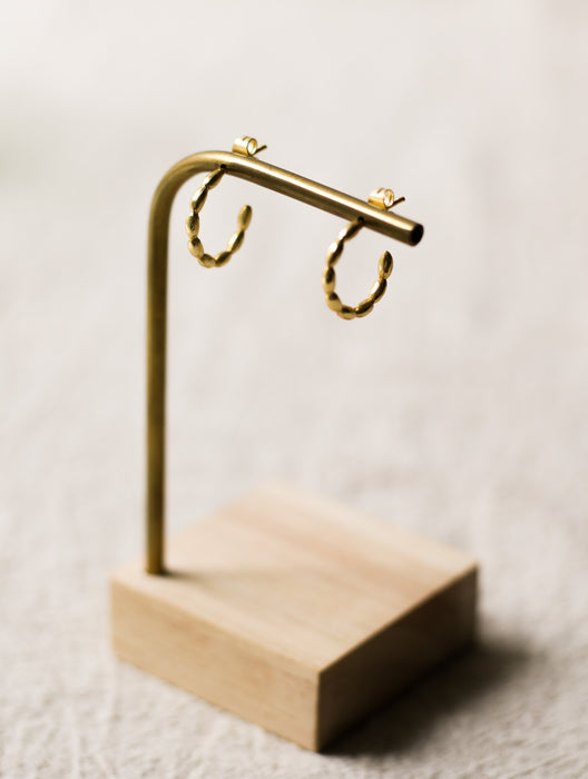 Gold hoop earrings on a wooden stand against a neutral linen background