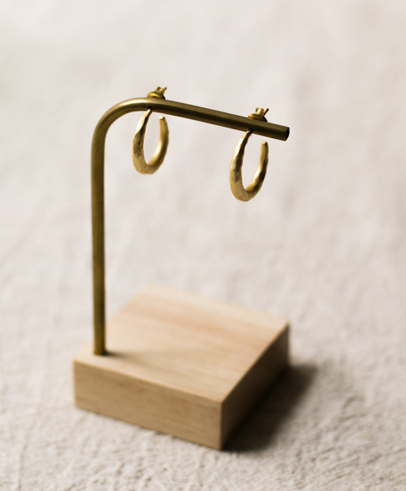 Gold hoop earrings on a wooden stand against a light linen background