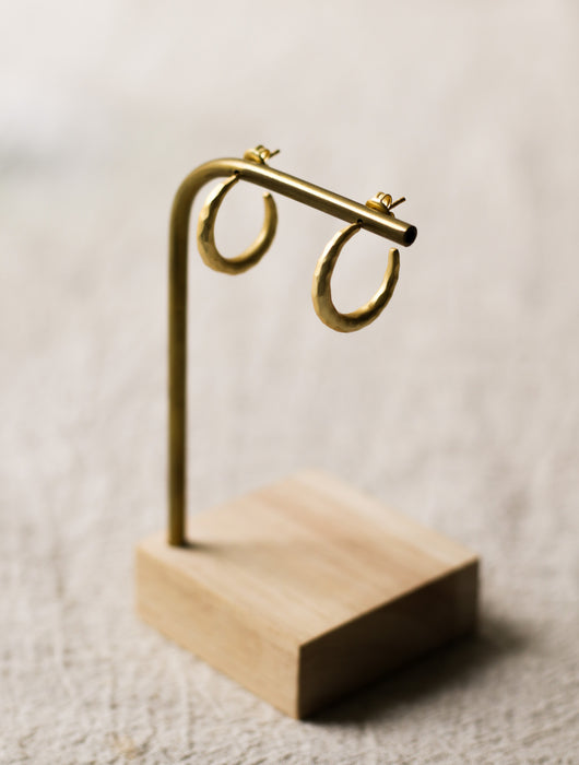 Gold hoop earrings on a wooden stand against a neutral linen background