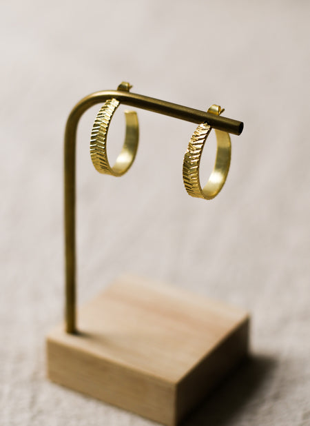 Gold hoop earrings on a wooden stand against a neutral background