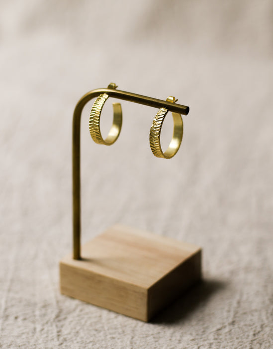 Gold hoop earrings on a wooden stand against a beige linen background