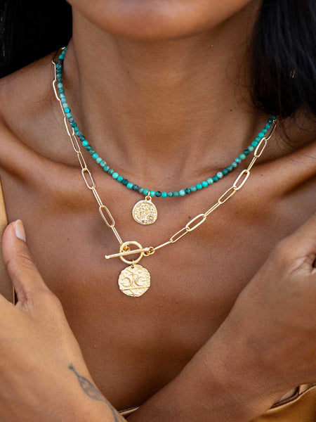 Close-up of a person wearing gold and turquoise necklaces.
