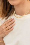 Close-up of a person wearing gold jewellery including a necklace, rings, and bracelets, and a white t shirt