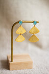 Gold fan detail earrings with aqua stones on a wooden stand against a neutral background
