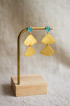 Gold fan detail earrings with aqua stones on a wooden stand against a neutral background