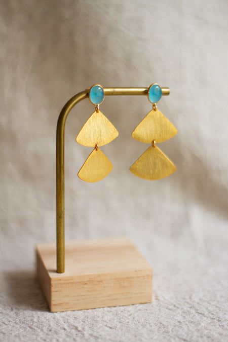 Gold fan detail earrings with aqua stones on a wooden stand against a neutral background