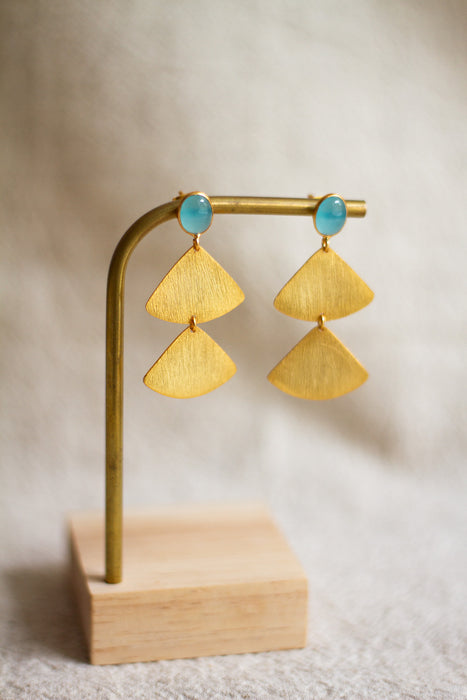 Gold fan detail earrings with aqua stones on a wooden stand against a neutral background
