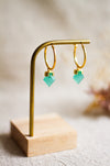 Gold hoop earrings with aqua gemstones on a wooden stand against a neutral background