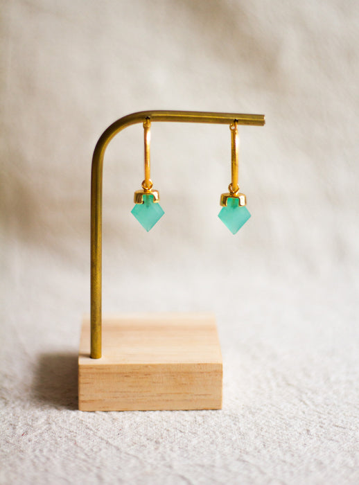 Gold earrings with aqua chalcedony stones on a wooden stand against a neutral background