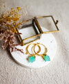 Gold hoop earrings with aqua stones on a white plate with dried flowers and a brass jewellery box.