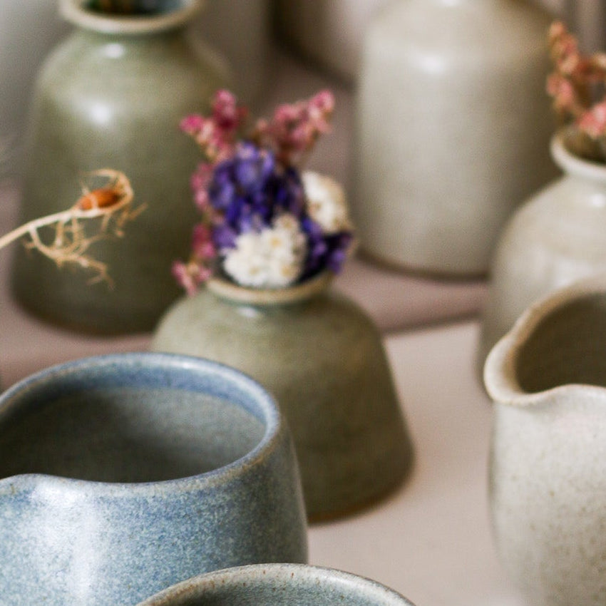 Collection of ceramic pitchers and vases WITH DRIED FLOWERS on a light surface with blurred background