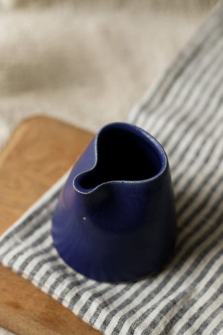 Blue ceramic pitcher on a striped tea towel and wooden bread board