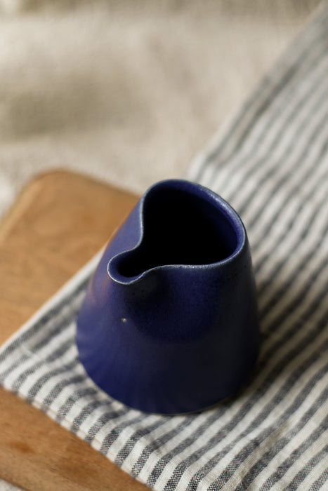 Blue ceramic pitcher on a striped tea towel and wooden bread board