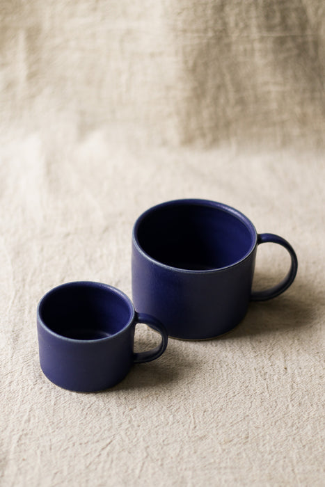 Two blue ceramic mugs on a beige textured surface