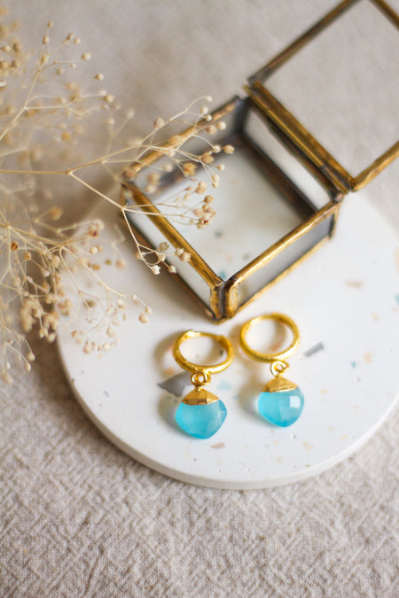 Gold hoop earrings with aqua drops on a white plate with dried flowers and a gold box.