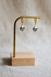 Pair of hoop earrings with labradorite gemstones on a gold earring stand against a neutral background