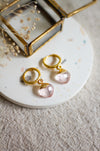 Gold hoop earrings with rose quartz gemstones on a white surface with dried flowers.