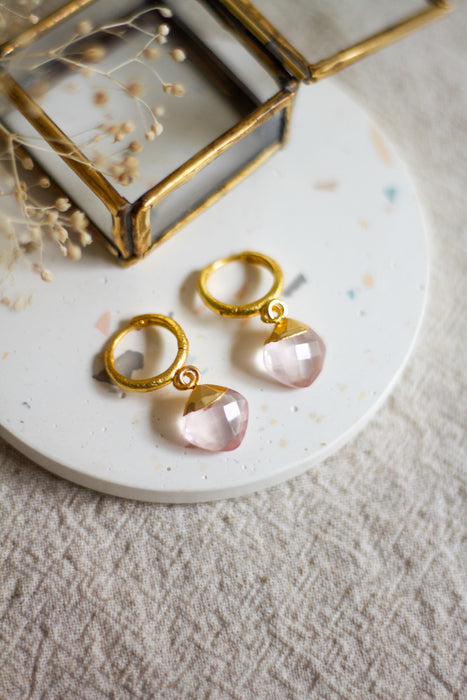 Gold hoop earrings with rose quartz gemstones on a white surface with dried flowers.