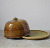 Brown ceramic butter dish on a light grey surface with a grey background