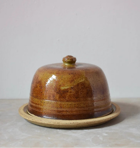 Brown ceramic butter dish on a light grey surface with a grey background