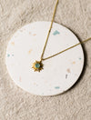 Gold necklace with a sun pendant on a round, speckled coaster on a beige linen surface