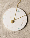 Gold necklace with a sun pendant on a round, speckled coaster on a beige linen surface