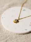 Gold necklace with a sun pendant on a round, speckled coaster.