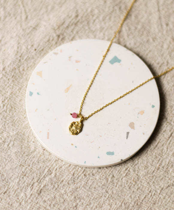Gold necklace with a pendant on a round, speckled stone surface