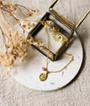 Gold necklace with a pendant on a speckled white coaster with dried flowers and a glass jewellery box