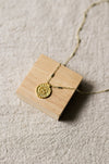 Gold necklace with a disc pendant on a wooden stand on a beige linen background
