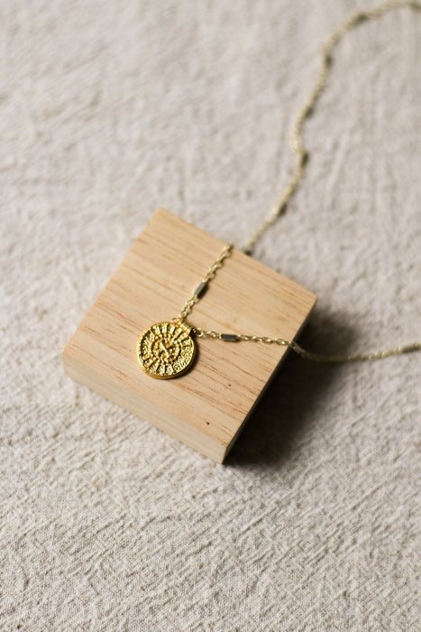 Gold necklace with a disc pendant on a wooden stand on a beige linen background